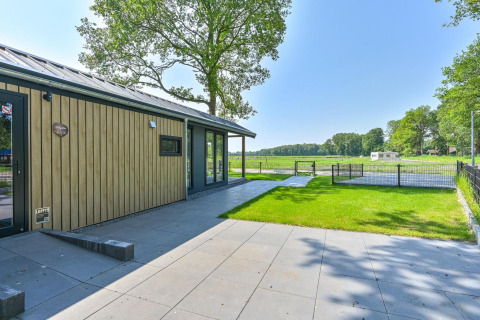 Buitenaanzicht van de rolstoeltoegankelijke Luxury Lodge bij Drentse Weelde met uitzicht op grasveld.