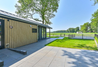 Buitenaanzicht van de rolstoelvriendelijke Luxury Lodge aan Drentse Weelde met zicht op het grasveld.
