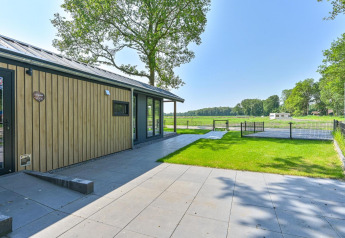 Buitenaanzicht van de rolstoelvriendelijke Luxury Lodge aan Drentse Weelde met zicht op het grasveld.