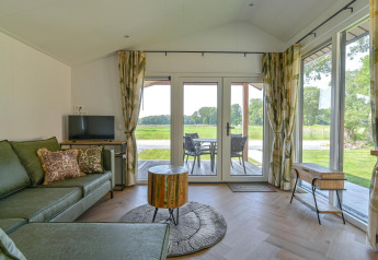 Woonkamer van een luxe lodge bij Drentse Weelde, Nederland, met groene zetel en zicht op natuur.