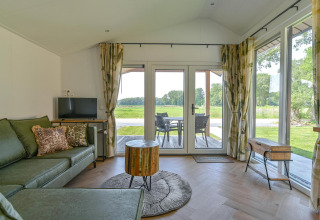 Salon d’un lodge de luxe à Drentse Weelde, Pays-Bas, avec canapé vert et vue sur la terrasse et la nature.