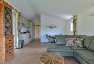 Luxe rolstoeltoegankelijke lodge in Drentse Weelde, Nederland, met grote groene zetel en open keuken.