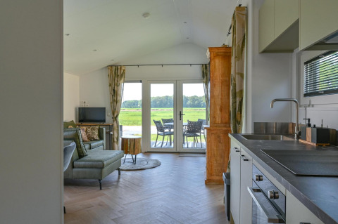 Cocina moderna y sala de estar con acceso a terraza y vista al campo en la Drentse Weelde lodge.