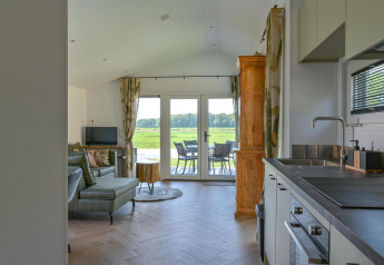 Modern kitchen and cozy living area with terrace and scenic countryside view at Drentse Weelde lodge.