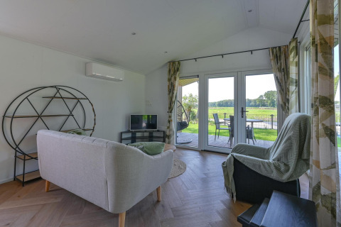 Stue i luksuslodge ved Drentse Weelde, Nederlandene, med moderne møbler og udsigt til grøn natur.
