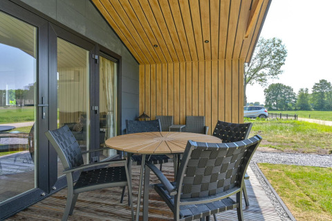 Terraza exterior con mesa redonda de madera y sillas negras en Luxury Lodge - accesible para sillas de ruedas, Drentse Weelde, Países Bajos.