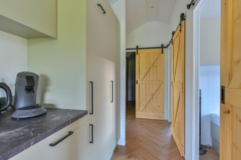 Corridoio moderno con porte scorrevoli in legno e cucina in un lodge accessibile alle sedie a rotelle a Drentse Weelde, Paesi Bassi.