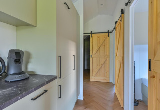 Moderne gang met schuifdeuren en keukenruimte in rolstoeltoegankelijke lodge bij Drentse Weelde, Nederland.