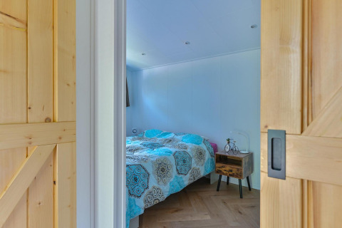 Dormitorio con cama doble, mesa de noche y puertas correderas de madera en un lodge accesible en Drentse Weelde.