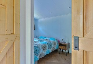 Dormitorio con cama doble, mesa de noche y puertas correderas de madera en un lodge accesible en Drentse Weelde.