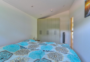 Slaapkamer met patroon dekbed, kledingkast en uitzicht op keuken in Luxury lodge bij Drentse Weelde.