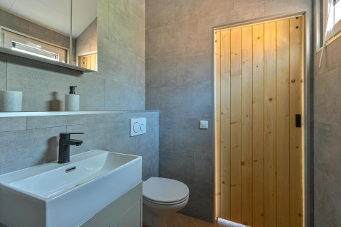 Modern badkamer met houten deur, strak sanitair en rolstoeltoegankelijk toilet in een luxe lodge te Drenthe.