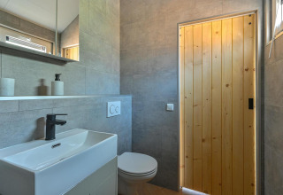 Bagno moderno con porta in legno, lavabo elegante e toilette accessibile in una luxury lodge nei Paesi Bassi.
