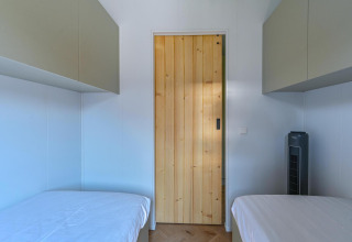 Twee bedden met witte lakens en een houten deur in de Luxury lodge - rolstoeltoegankelijk bij Drentse Weelde.