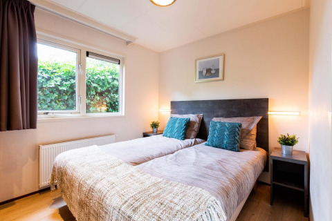 Helles Schlafzimmer mit zwei Einzelbetten, Pflanzen und großem Fenster im Holiday home bei EuroParcs Noordwijkse Duinen.