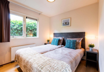 Helles Schlafzimmer mit zwei Einzelbetten, Pflanzen und großem Fenster im Holiday home bei EuroParcs Noordwijkse Duinen.