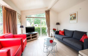Helles Wohnzimmer mit roten Sesseln, grauem Sofa und großen Fenstern im Ferienhaus EuroParcs Noordwijkse Duinen.