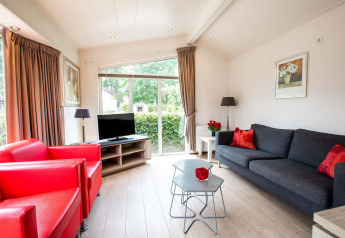 Salon lumineux avec fauteuils rouges, canapé gris et grande baie vitrée dans un gîte à EuroParcs Noordwijkse Duinen.