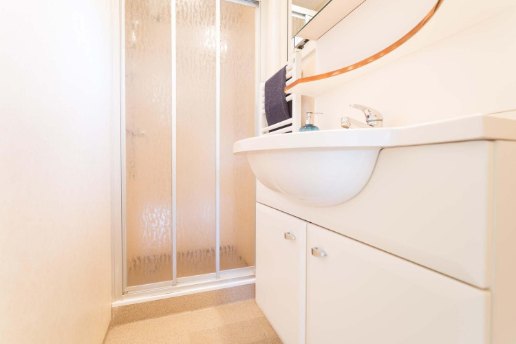 Baño moderno con ducha y lavabo blanco en una casa de vacaciones en EuroParcs Noordwijkse Duinen, Países Bajos.