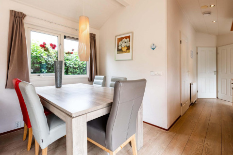 Lichte eetruimte in een vakantiehuisje met moderne stoelen, een bloemenvaas en schilderij aan de muur.
