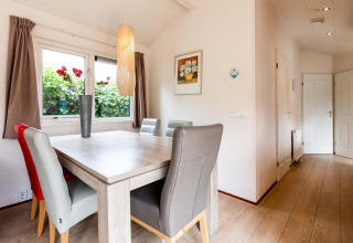 Lichte eetruimte in een vakantiehuisje met moderne stoelen, een bloemenvaas en schilderij aan de muur.