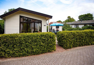 Ferienhaus im EuroParcs Noordwijkse Duinen in den Niederlanden mit Terrasse, Hecke und Gästen draußen.