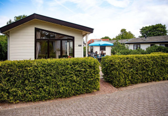 Feriehytte ved EuroParcs Noordwijkse Duinen i Holland, med terrasse, hæk og folk under en blå parasol.