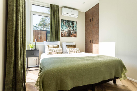 Chambre lumineuse dans un lodge avec rideaux verts, lit double et tableau de cerf au-dessus du lit.