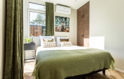 Dormitorio luminoso en una cabaña con cortinas verdes, cama doble y cuadro de naturaleza sobre la cama.