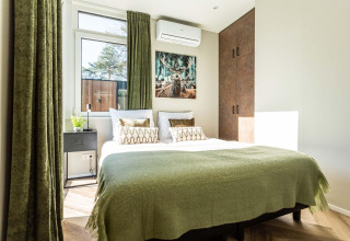 Bright bedroom in a lodge with green curtains, double bed, decorative pillows and nature artwork above.