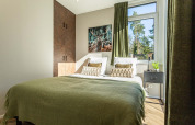 Cozy lodge bedroom with a double bed, green bedspread, nature view through window, and deer artwork.