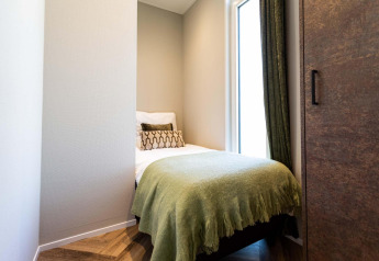 Petite chambre moderne d’un lodge avec lit simple, couverture verte et grande fenêtre à rideaux.