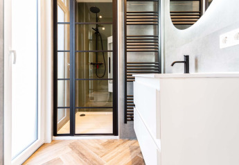Salle de bain moderne dans un lodge avec porte de douche en verre, robinet noir et meuble blanc sur parquet.