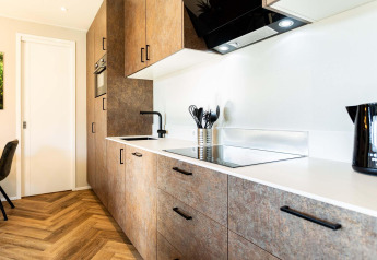 Cucina moderna in lodge con pavimento effetto legno, piano bianco e accessori neri incorporati.