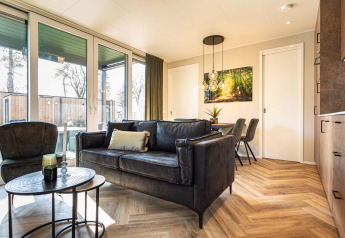 Heldere, moderne lodge woonkamer met grote ramen, houten vloer en eigentijds zwart meubilair.