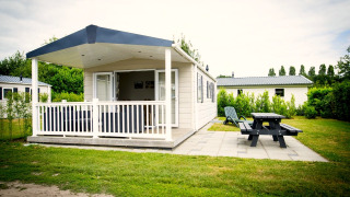 Tiny house Forest Lodge ved Holiday Park Duinhoeve med veranda, bænk og grønt område i Nederlandene.