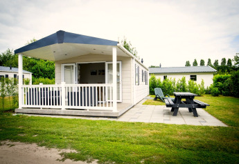 Tiny house named Forest Lodge at Holiday Park Duinhoeve, Netherlands, featuring a porch, bench, and greenery.