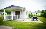Tiny house Forest Lodge en Holiday Park Duinhoeve, Países Bajos, con porche, banco y zona verde.