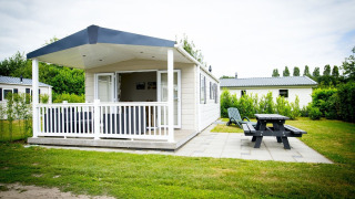 Tiny house Forest Lodge en Holiday Park Duinhoeve, Países Bajos, con porche, banco y zona verde.