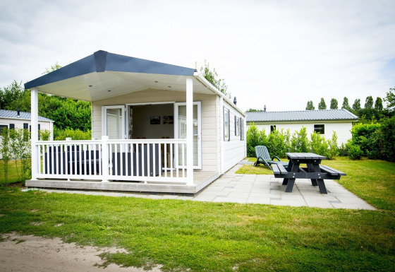 Tiny house Forest Lodge en Holiday Park Duinhoeve, Países Bajos, con porche, banco y zona verde.