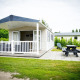 Tiny house Forest Lodge en Holiday Park Duinhoeve, Países Bajos, con porche, banco y zona verde.