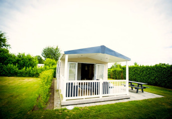 Tiny house with covered porch and bench at Forest Lodge, Holiday Park Duinhoeve, Netherlands, surrounded by greenery.