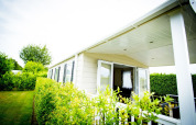Forest Lodge tiny house presso Holiday Park Duinhoeve, Paesi Bassi, con veranda coperta e siepe.