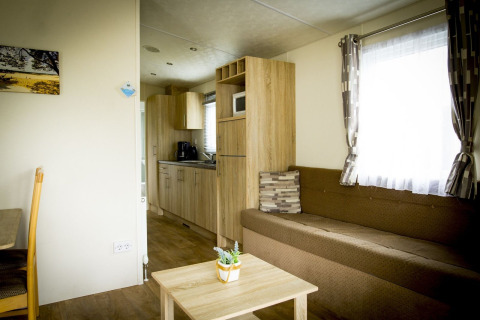 Woonruimte en keuken van Forest Lodge tiny house in Holiday Park Duinhoeve met bank, tafel en modern interieur.