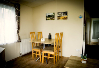 Dining area inside Forest Lodge at Holiday Park Duinhoeve, Netherlands, with table and four wooden chairs
