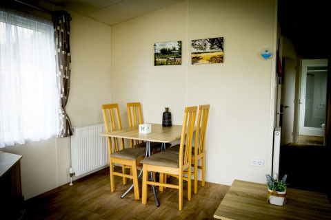 Eethoek in Forest Lodge bij Holiday Park Duinhoeve, Nederland, met tafel en vier houten stoelen bij raam