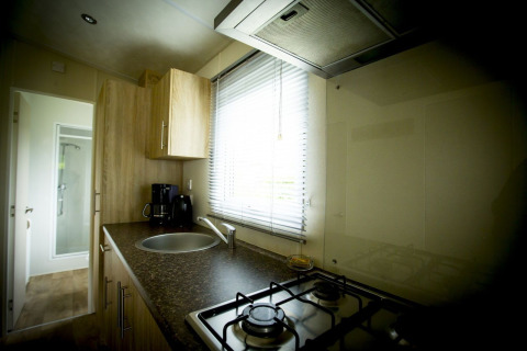 Cocina pequeña en Forest Lodge, Holiday Park Duinhoeve, Países Bajos, con fogón de gas y fregadero.