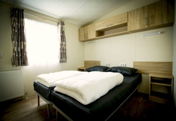 Bedroom at Forest Lodge, Holiday Park Duinhoeve, Netherlands with a double bed, curtains, and wood furniture.