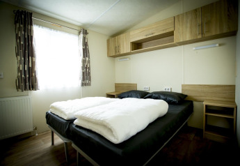 Schlafzimmer im Forest Lodge, Holiday Park Duinhoeve, Niederlande mit Doppelbett und Holzmöbeln.