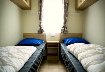 Small twin bedroom with two single beds, window and wooden cabinets at Forest Lodge, Holiday Park Duinhoeve.
